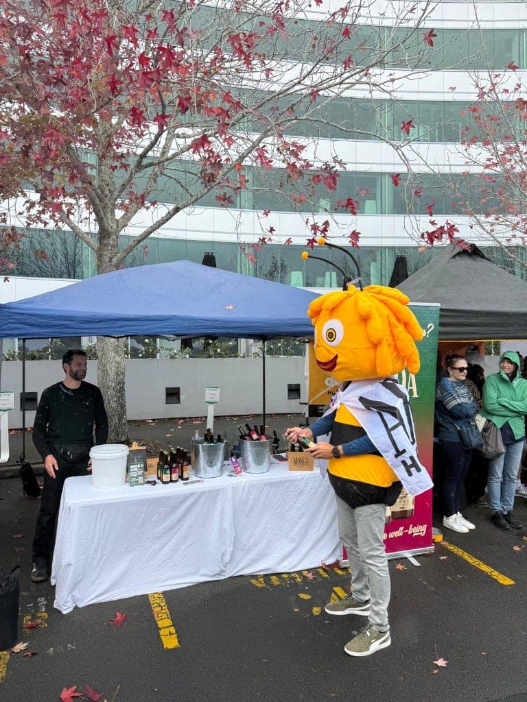 The Aroā bee mascot holding a bottle of Berries Jun in the sun